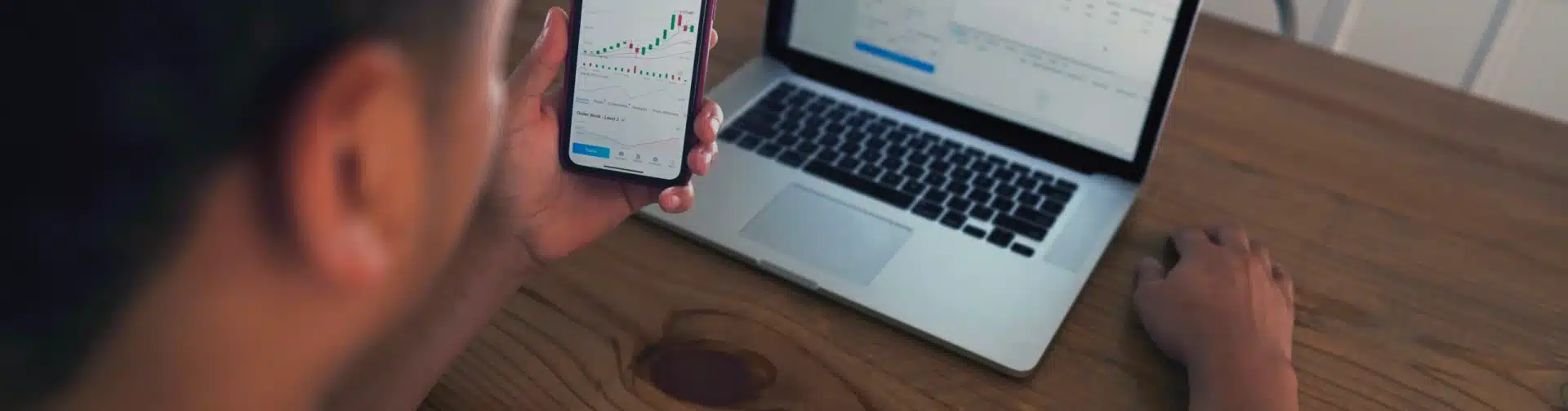 Person analyzing financial charts on smartphone and laptop