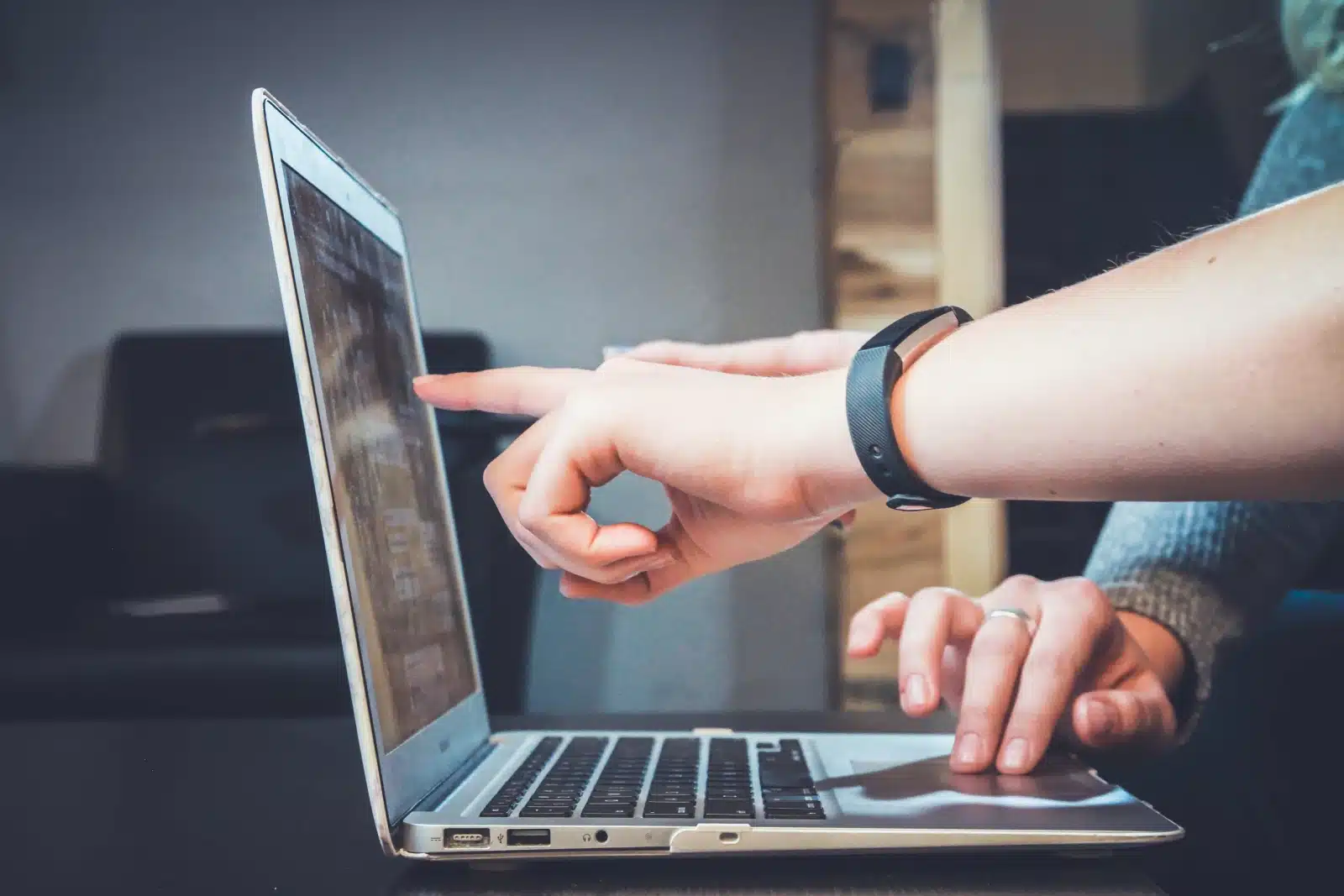 Person using laptop computer with fitness tracker, hands positioned over keyboard and trackpad