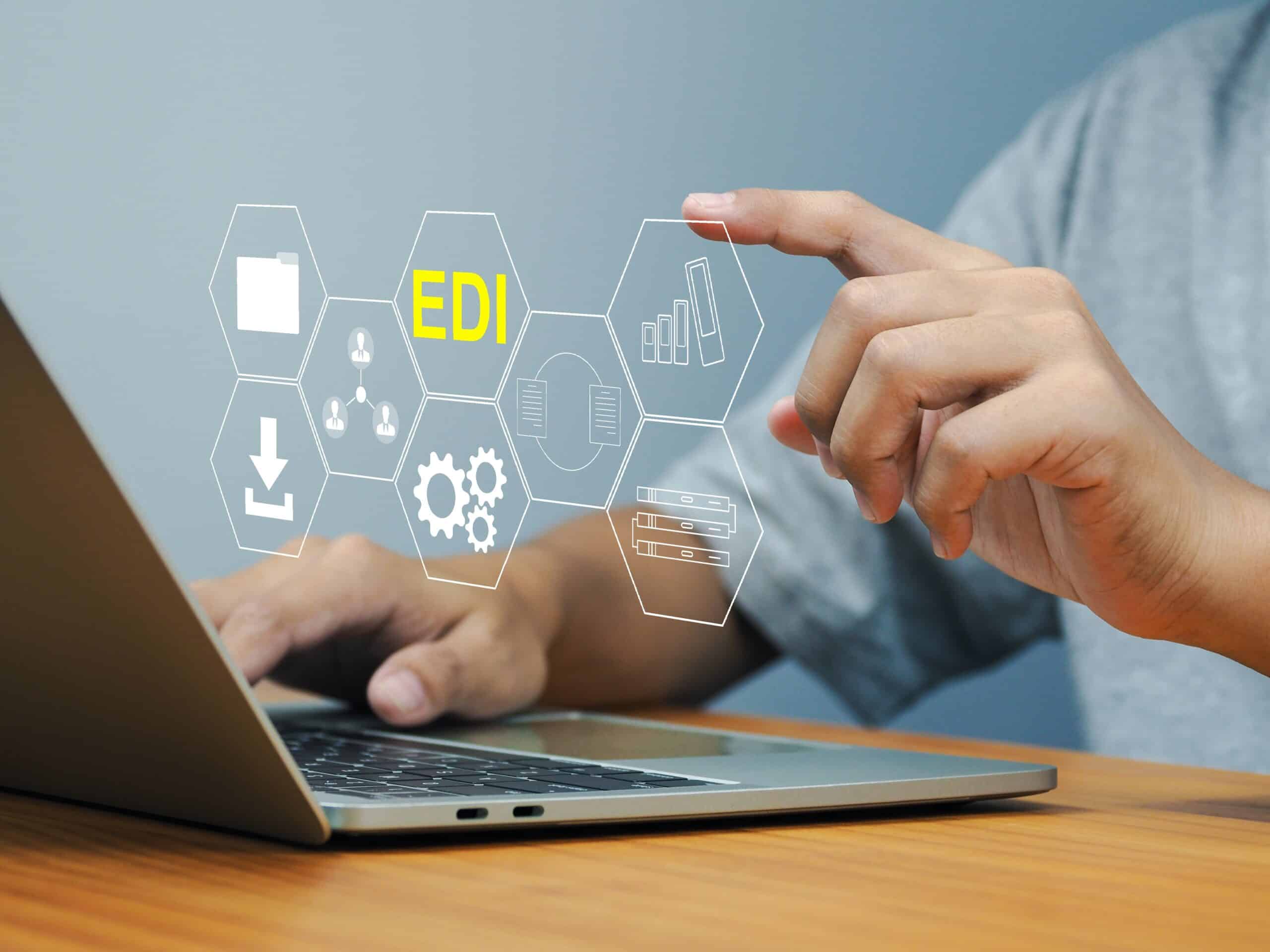 Hand near a laptop with an EDI-themed graphic overlay showing icons for files, people, gears, and servers