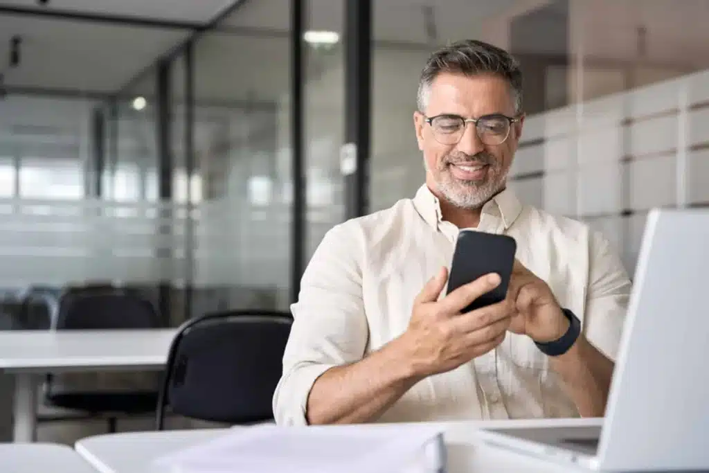 Businessman smiling while using smartphone for digital payments in modern office