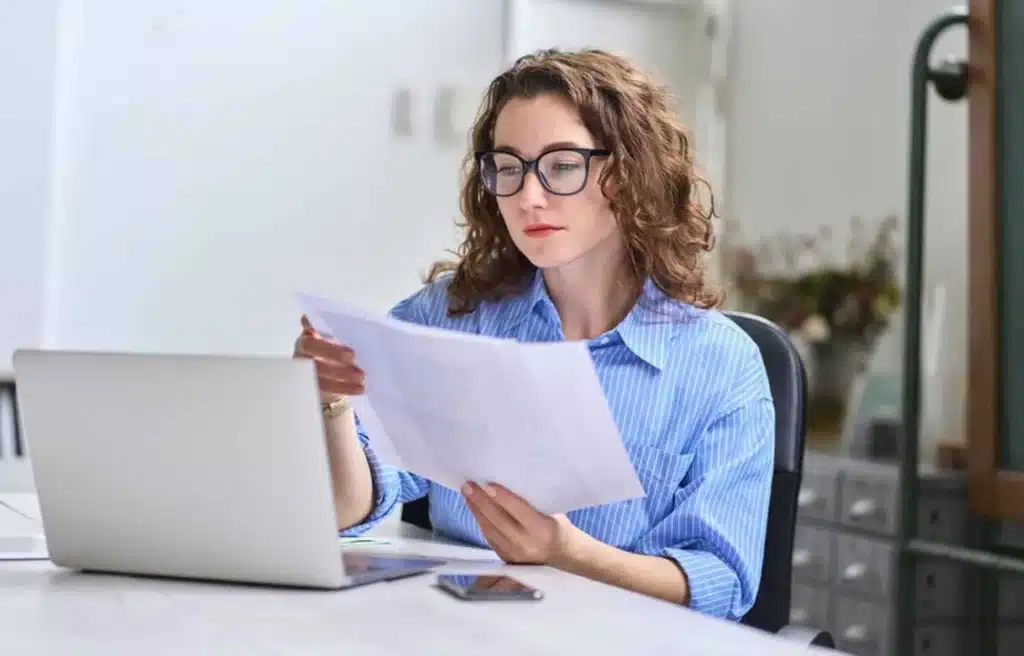 Professional woman reviewing business documents at desk with laptop for payment processing