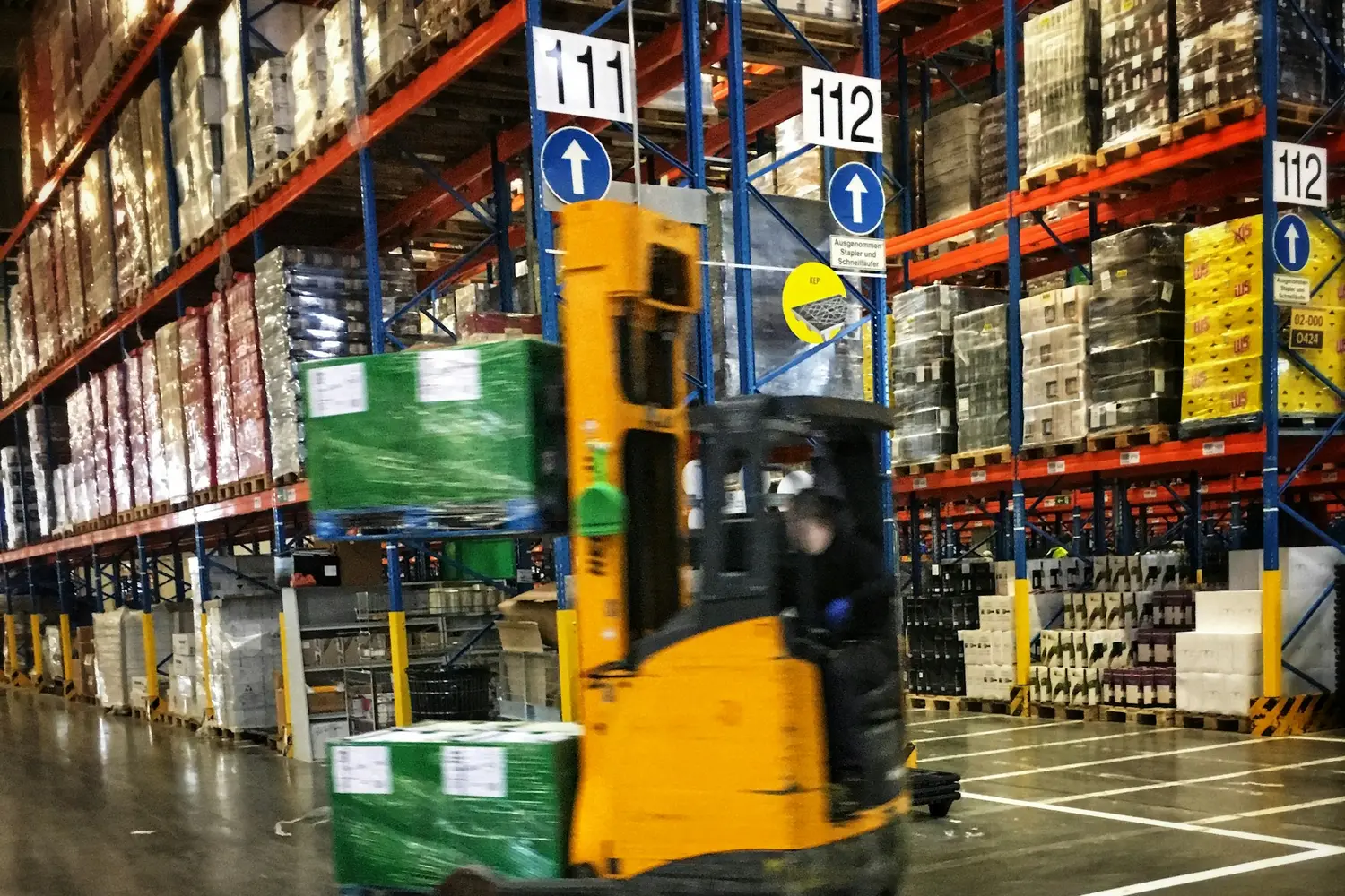 Forklift moving between pallet racks in a warehouse aisle