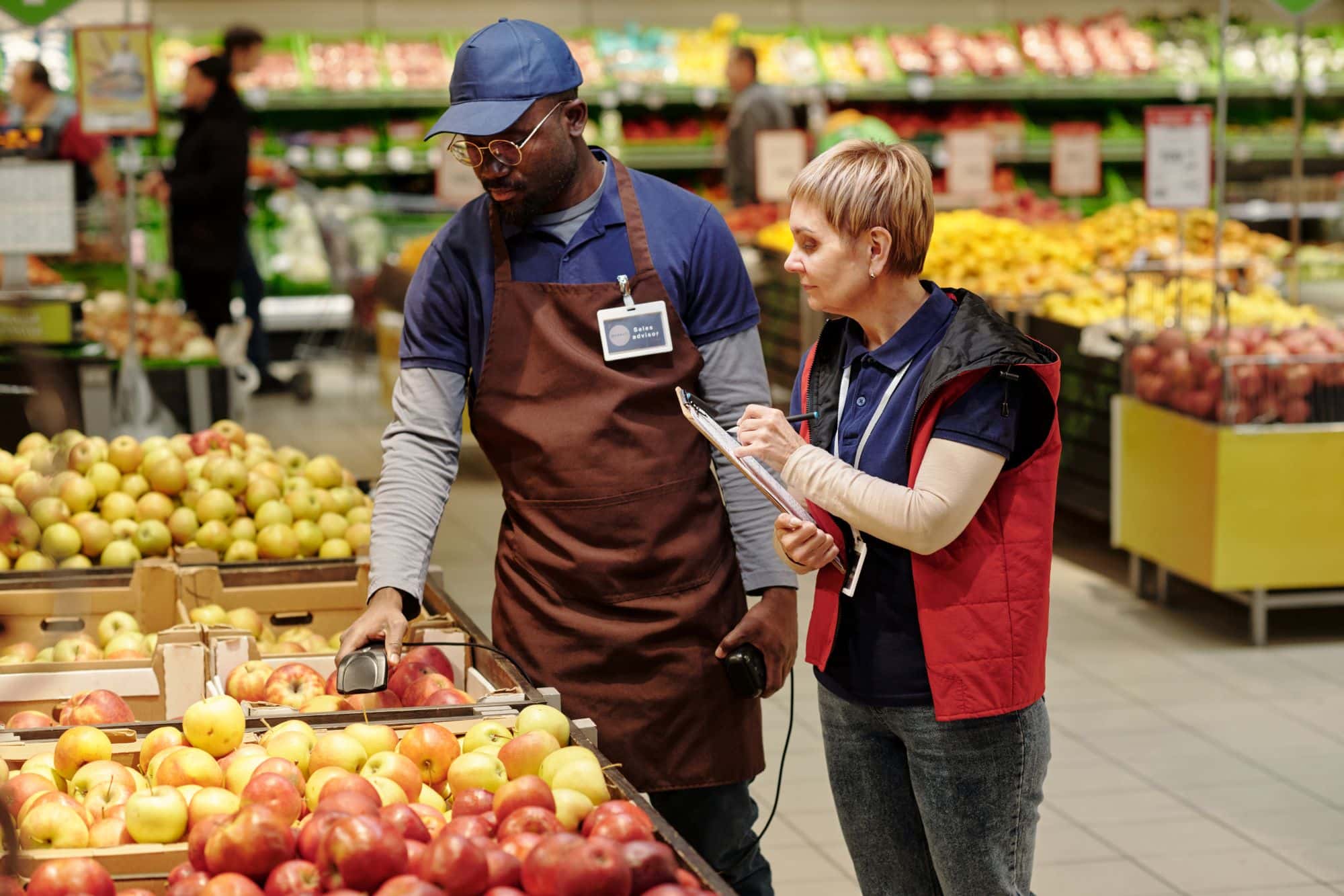 Mature sales advisor taking notes while a colleague holds fruit