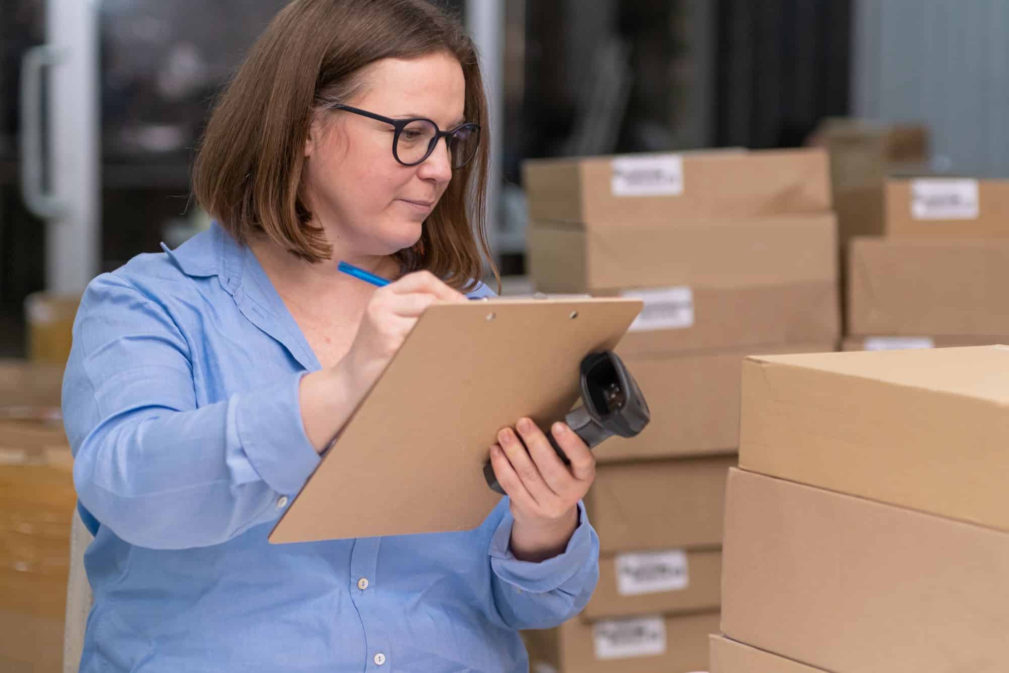 Small business owner checking off items for shipment while holding a barcode scanner