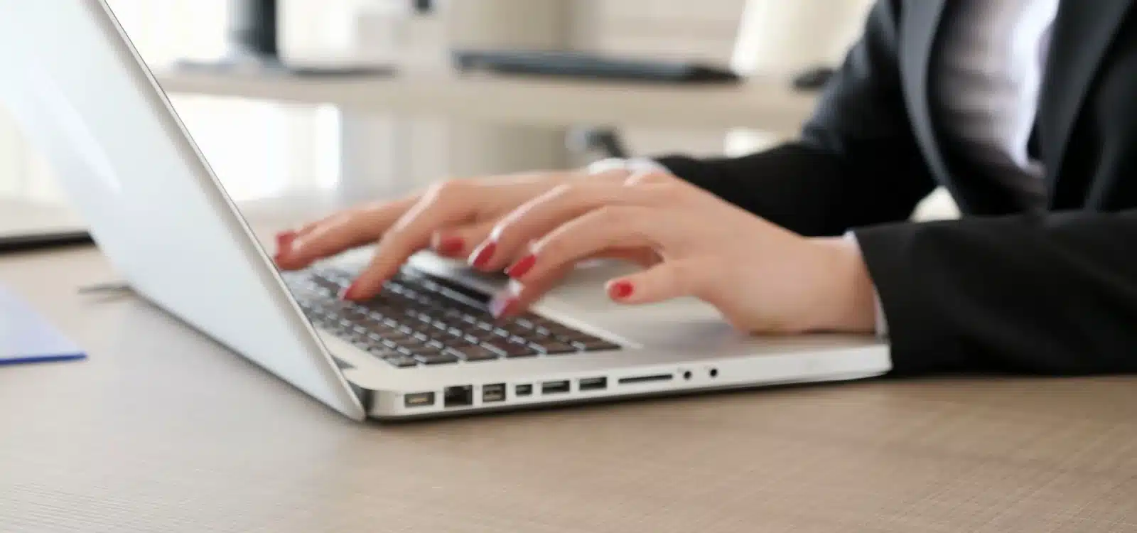 Woman typing on silver laptop computer at modern office desk