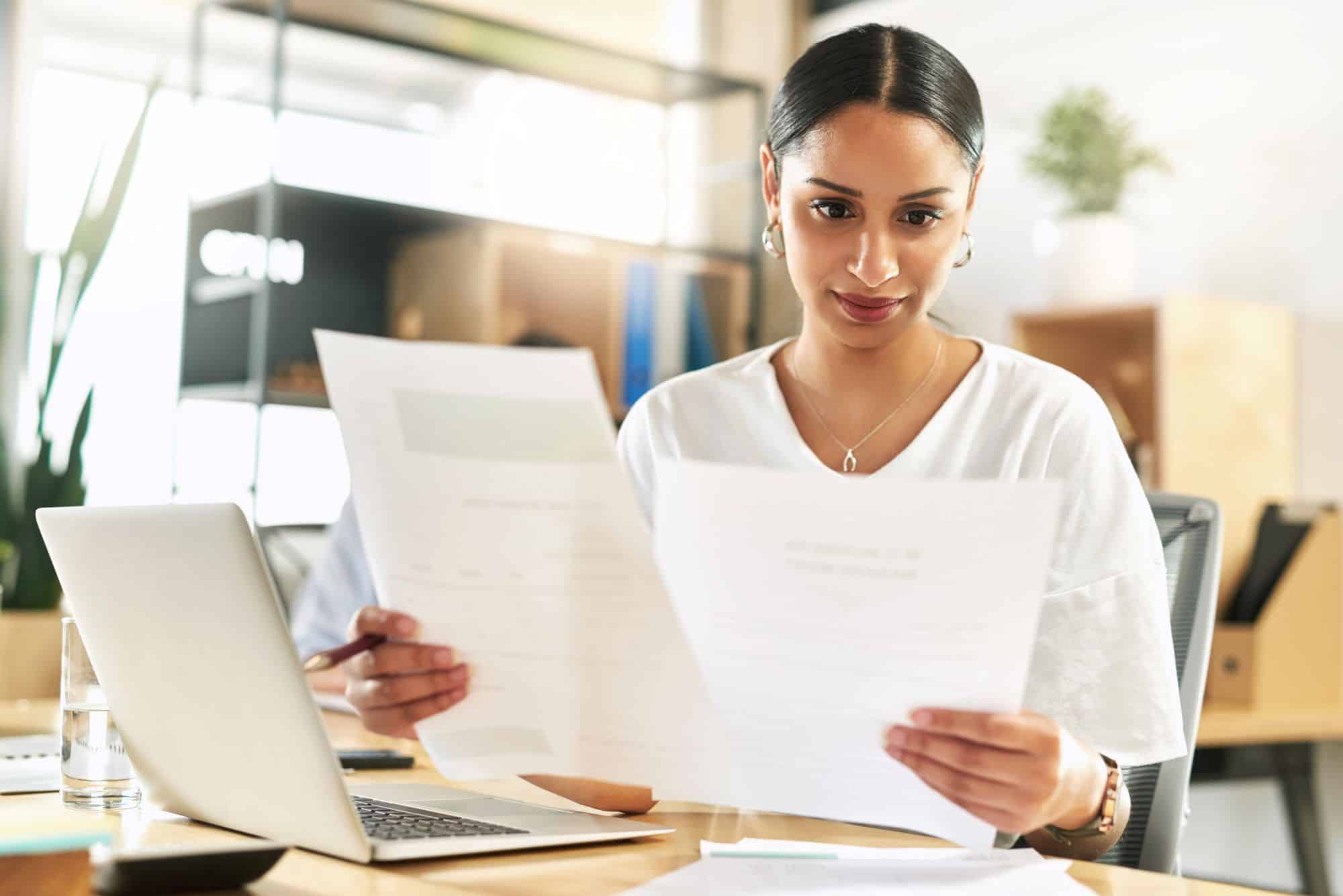 Woman comparing documents at a desk with a laptop
