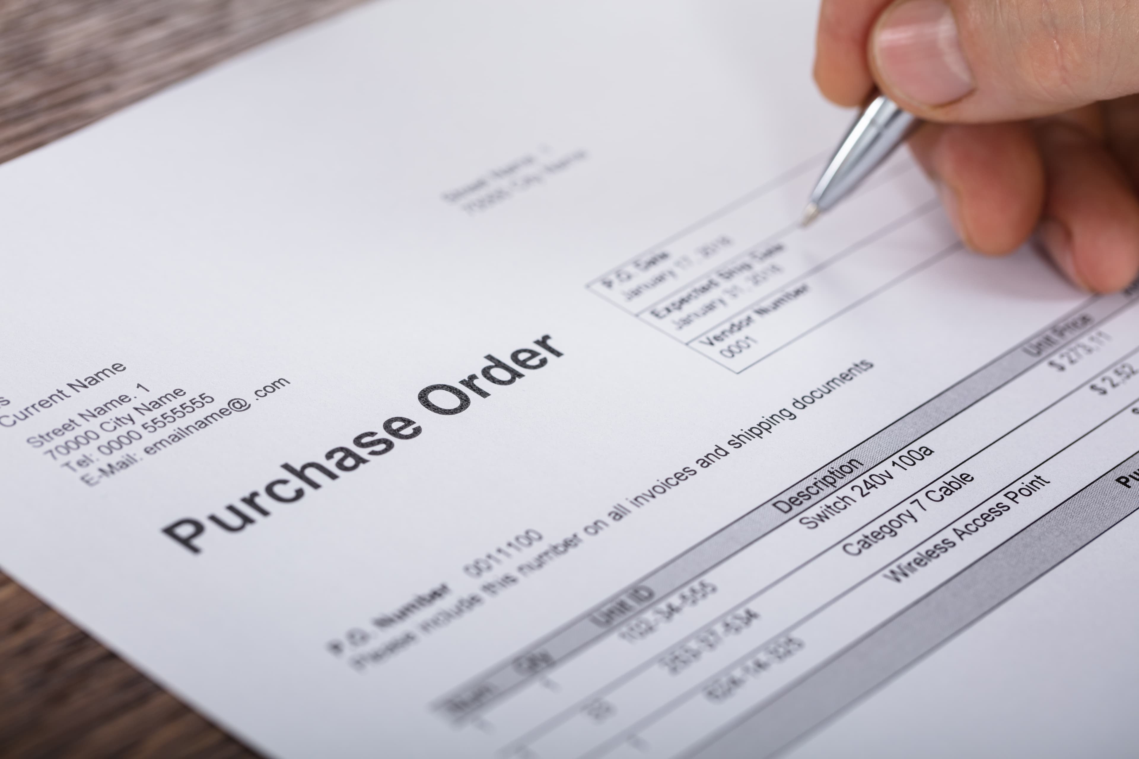 Close-up of a purchase order form listing networking equipment, with a pen pointing to the order date