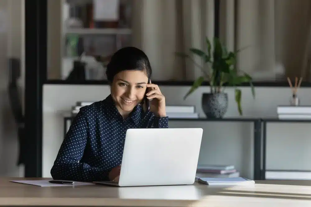 Professional woman working on laptop while talking on phone in modern office