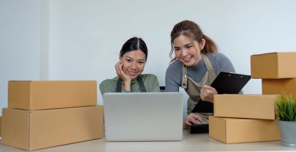 two women looking at a laptop on a table full of boxes